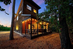 Une cabane en rondins avec un porche, une cheminée et des guirlandes lumineuses.