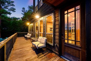 Une terrasse en bois avec des sièges d’extérieur, de grandes fenêtres et une vue sur l’intérieur.