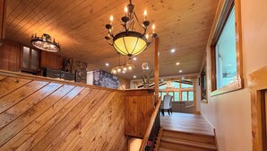 Un escalier en bois avec une rampe, un lustre et une vue sur un coin repas comprenant une table et des chaises.