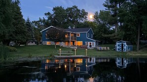 Une maison avec une jetée qui s’avance sur une étendue d’eau calme, entourée d’arbres.