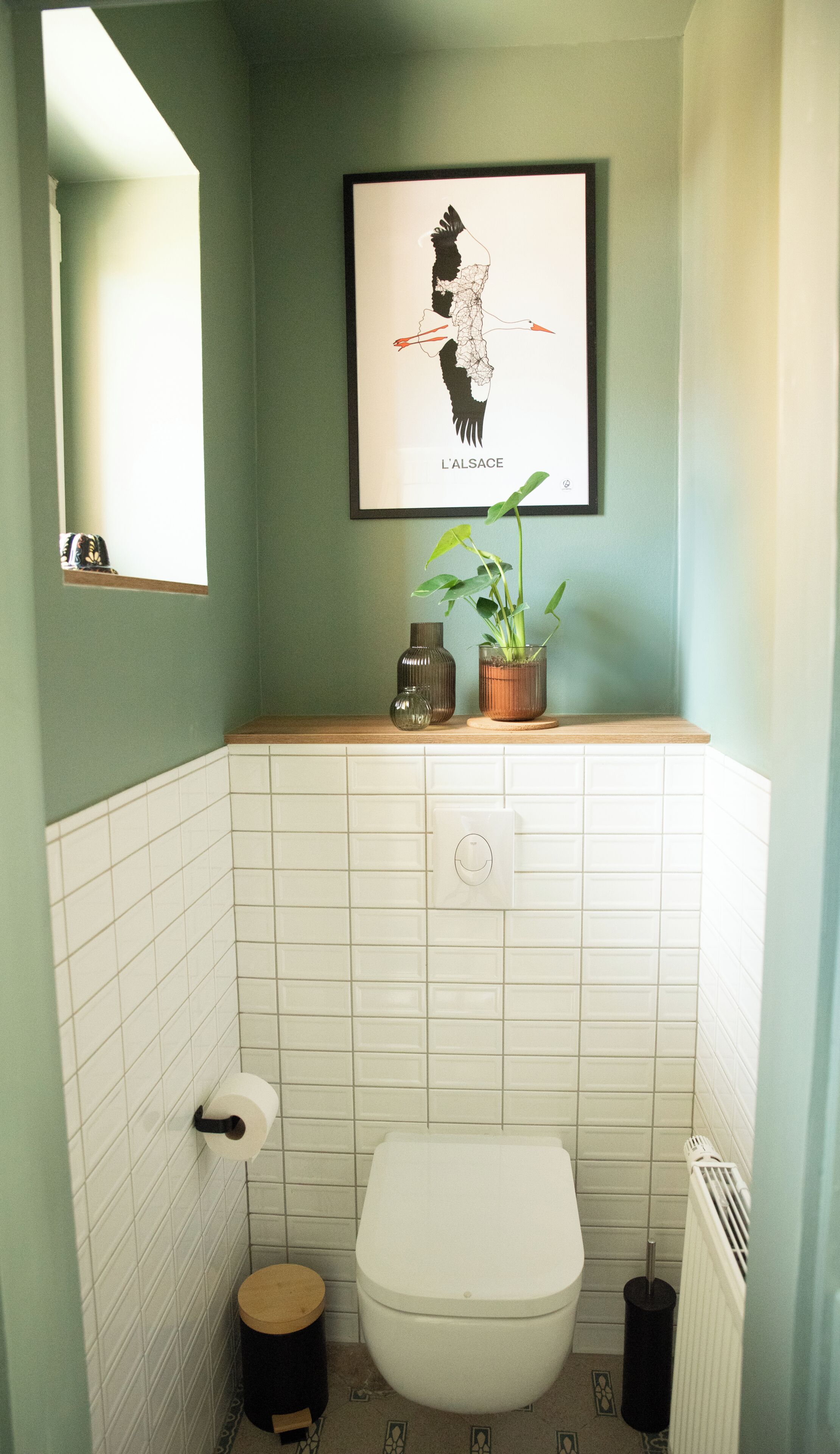 Un baño con inodoro, lavamanos con espejo, un mapa enmarcado y una planta en maceta.