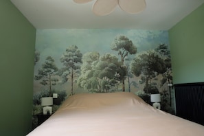 A bedroom with a bed, two bedside tables with lamps, a ceiling fan, and a mural of trees on the wall.