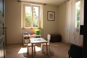 Una habitación con ventana, una mesa, sillas, un radiador y un cuadro en la pared.