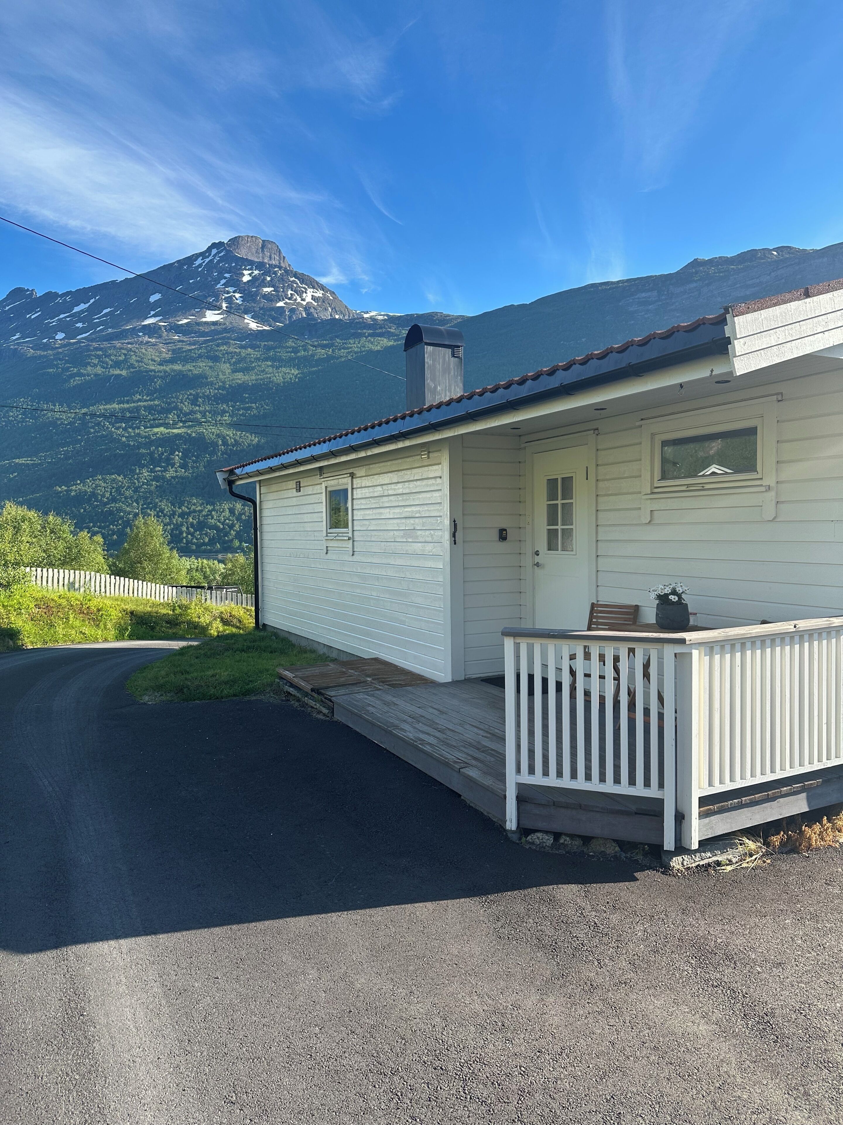 A white cabin with a porch, a mountain backdrop, and a clear sky.