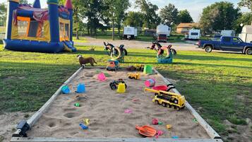 Un bac à sable avec des jouets et, au fond, une structure de jeu.