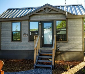 Een houten chalet met een metalen dak, een voordeur en een trap die naar de ingang leidt.