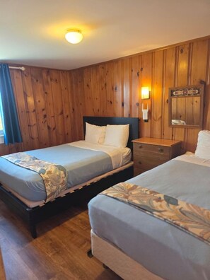 A room with two beds, wooden walls, a nightstand, and a wall-mounted light fixture. - Wake Up to the Sound of Waves by the Shore in North Truro, Massachusetts (North Truro)