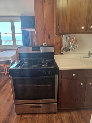 A kitchen with a stove, oven, wooden cabinets, and a window with a view. - Wake Up to the Sound of Waves by the Shore in North Truro, Massachusetts (North Truro)