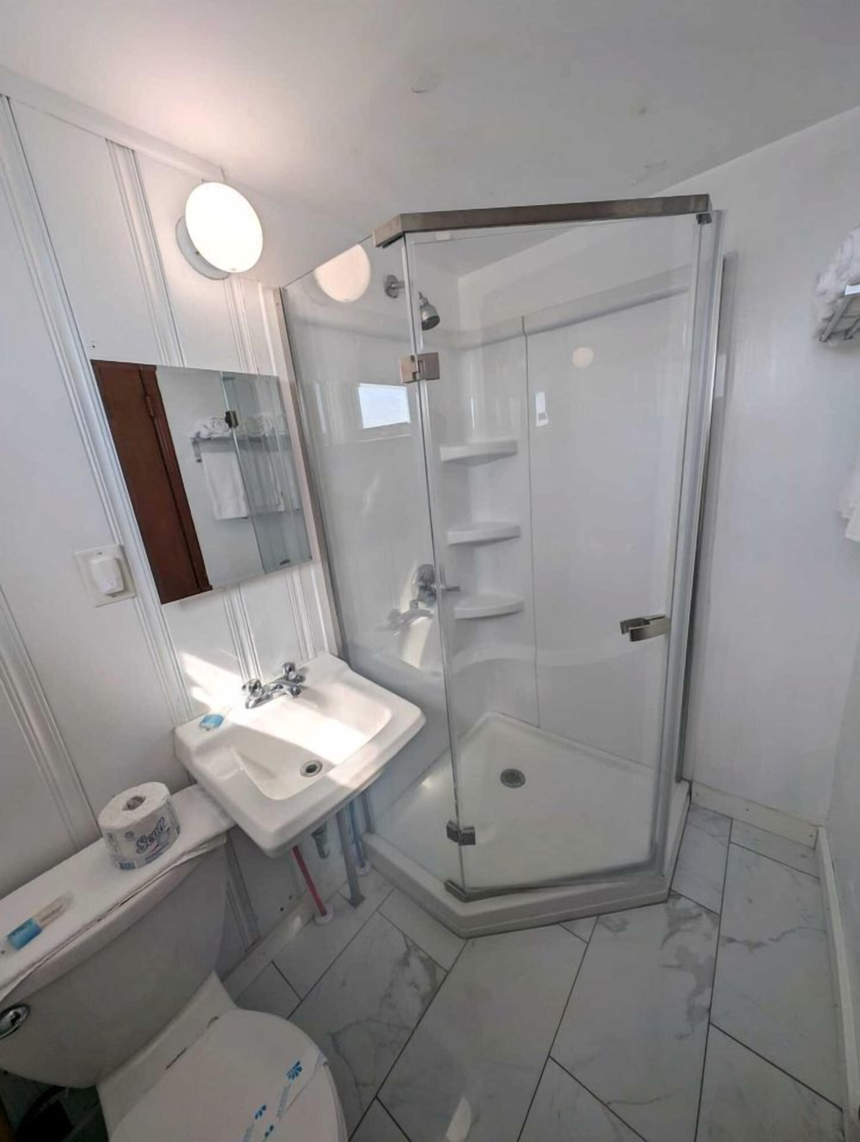 Un baño con cabina de ducha de vidrio, lavamanos blanco, espejo y inodoro.