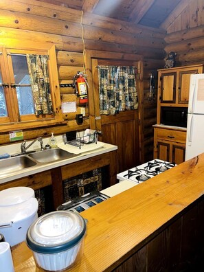A wooden cabin kitchen with a gas stove, sink, cabinets, and a fire extinguisher.