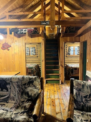 L’intérieur d’une cabane est agrémenté d’un escalier en bois, de deux canapés à motifs animaliers et d’une pancarte indiquant « Cabane n° 5 ».