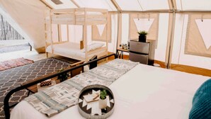 Alojamiento en tienda de campaña con cama, una mesita, una silla y un refrigerador.