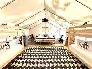 A tented room with bunk beds, a central bed, a patterned floor, and a hanging light fixture.
