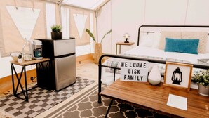 Una habitación acogedora con una cama, una mesita con un letrero de bienvenida, un refrigerador y una cafetera.