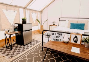 Een gezellige kamer met een bed, een klein tafeltje met een welkomstbord, een koelkast en een koffiezetapparaat.
