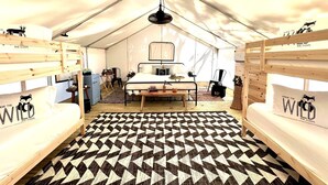 Una habitación con carpa, camas literas, una cama central, piso estampado y una lámpara colgante.