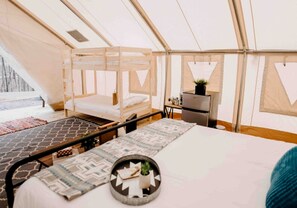 Een tentaccomodatie met een bed, een tafeltje, een stoel en een koelkast.