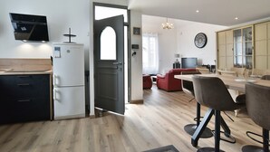 Een moderne keuken met een ingebouwde oven, een eethoek met een houten tafel en stoelen, en een woonkamer met een bank en een televisie.