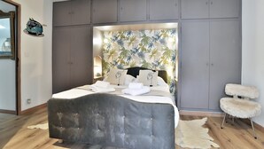 Een slaapkamer met een bed, een hoofdeinde met een bladmotief, een zachte fauteuil en een vachtkleed.