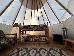 A cozy interior with a wooden bunk bed, a patterned rug, a small table, and a tent-like structure.