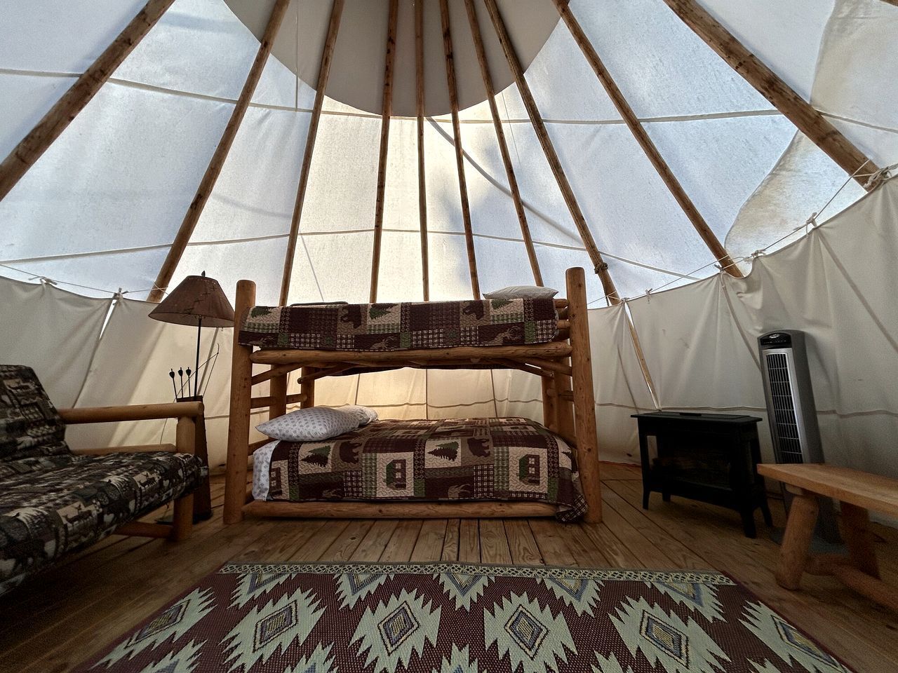 A cozy interior with a wooden bunk bed, a patterned rug, a small table, and a tent-like structure.