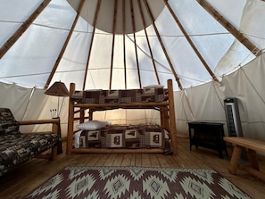 Un intérieur chaleureux avec un lit superposé en bois, un tapis à motifs, une petite table et une structure ressemblant à une tente.