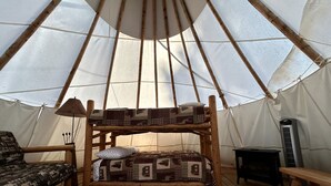 A cozy interior with a wooden bunk bed, a patterned rug, a small table, and a tent-like structure.