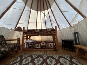 A cozy interior with a wooden bunk bed, a patterned rug, a small table, and a tent-like structure.