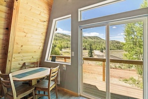 Ein Holzkamin mit Esstisch und Stühlen, große Fenster mit Blick auf eine bewaldete Landschaft.