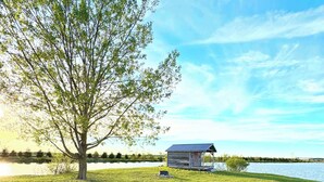 A lakeside cabin with a grassy lawn, a large tree, and a view of the lake. - South Cabins - Private Island (Perth County)