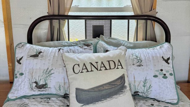 A bed with a view of a lake, a wooden ceiling, and a window with curtains. - South Cabins - Private Island (Perth County)