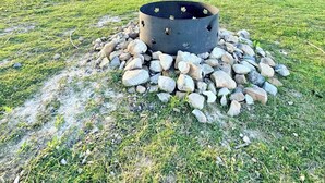 A rustic wooden cabin with a metal roof, a fire pit surrounded by rocks, and a grassy field with a clear sky. - South Cabins - Private Island (Perth County)