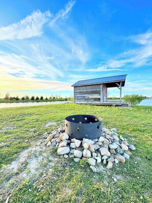 A rustic wooden cabin with a metal roof, a fire pit surrounded by rocks, and a grassy field with a clear sky. - South Cabins - Private Island (Perth County)