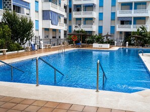 A swimming pool with a tiled deck, surrounded by a multi-story building with balconies. - La Luz de Chipiona by Apartments Time (Chipiona)