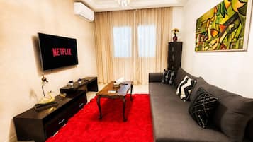 A living room with a flat-screen TV, a sofa, a coffee table, and a red rug.