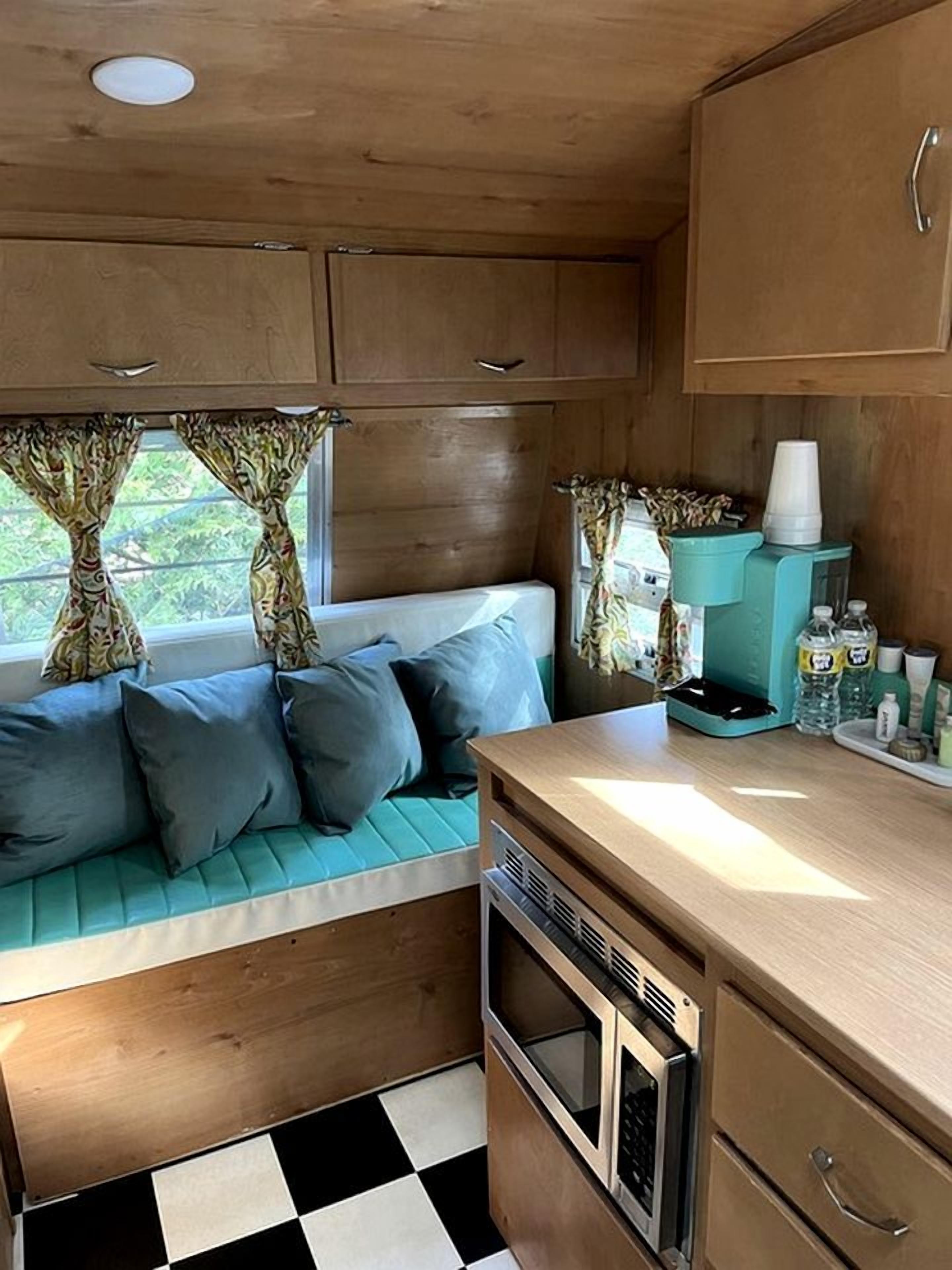A compact kitchen with a built-in microwave, a sink, and a window with curtains.