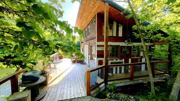A wooden deck leading to a cabin with a porch, surrounded by trees and a gravel path.