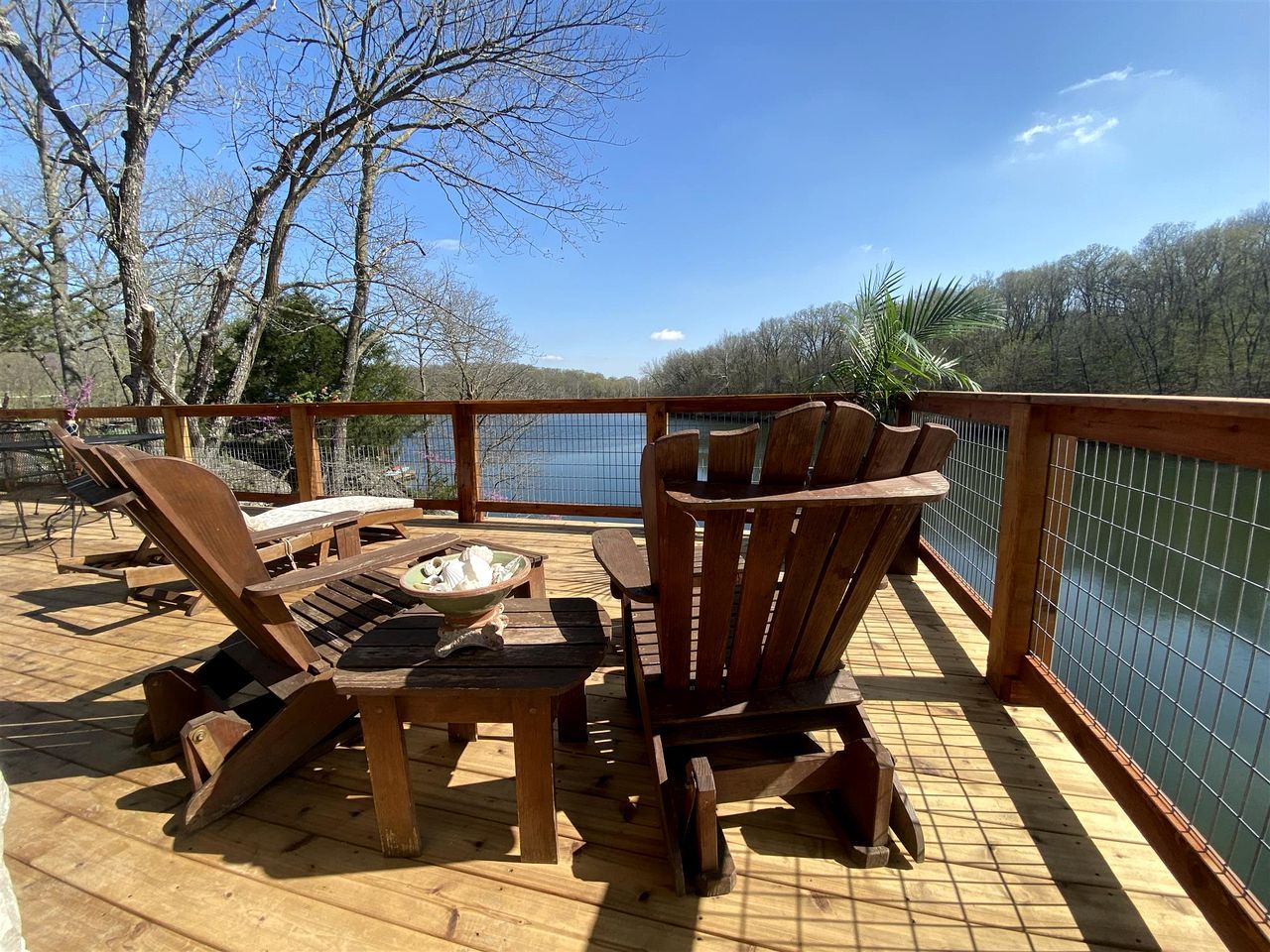 A wooden deck with lounge chairs and a table, overlooking a body of water.