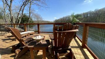A wooden deck with lounge chairs and a table, overlooking a body of water.
