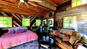 A log cabin interior with a bed, sofa, coffee table, and a ceiling fan.
