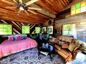 A log cabin interior with a bed, sofa, coffee table, and a ceiling fan.