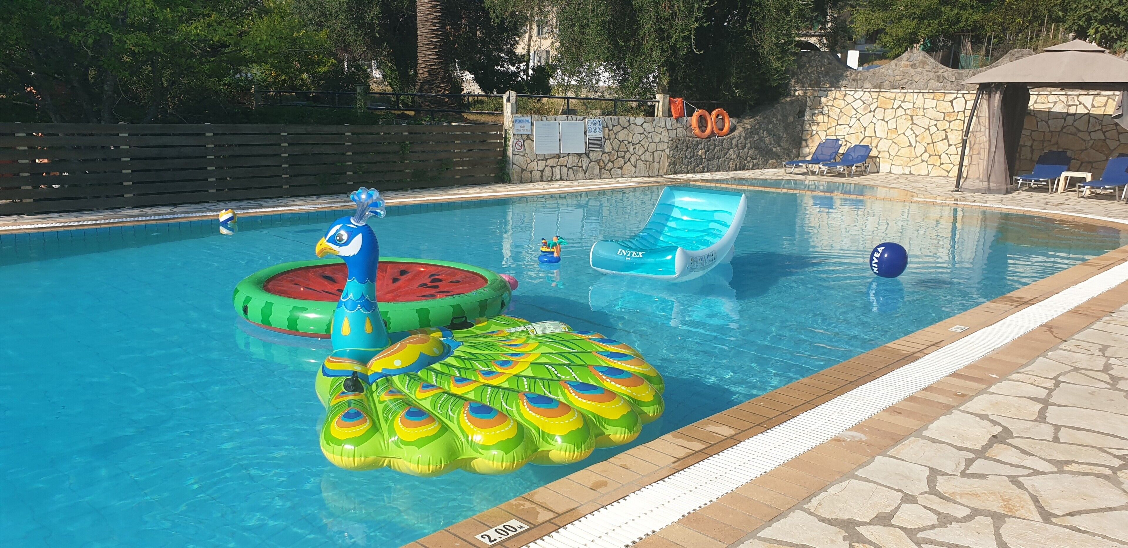En swimmingpool med oppustelige vandlege, liggestole og en stenvæg.