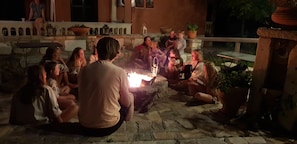 A group of people sitting around a fire pit in an outdoor setting with stone walls and potted plants. - Poolfront Cabana 13 – Small Double Room by the Pool (Kontokali)
