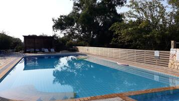 A swimming pool with a tiled deck, lounge chairs, and a wooden fence.