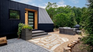 A modern black building with a wooden door, steps leading to a stone pathway, and outdoor furniture. - Blissful A-Frame Retreat near Pisgah National Forest in North Carolina (Balsam Grove)