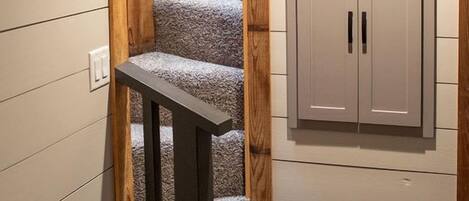 A staircase with a wooden finish, a grey carpeted landing, and a set of cabinets with two doors.
