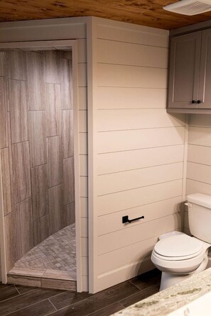 Baño con ducha, inodoro y suelo de madera.