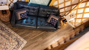 A modern living room with a leather sofa, patterned cushions, a woven basket, and a wooden floor.