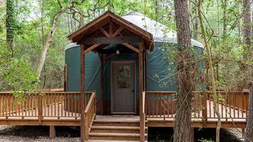 A yurt with a wooden porch and a door, surrounded by trees.
