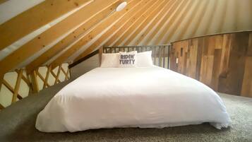 A bed in a loft bedroom with a sloped ceiling and wooden beams.